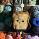 Photo of crocheted bag in shape of sliced sandwich bread with face, arms, and legs